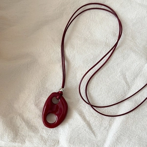 Macro shot of dark red oval resin pendant with a glossy finish on woven textile cord