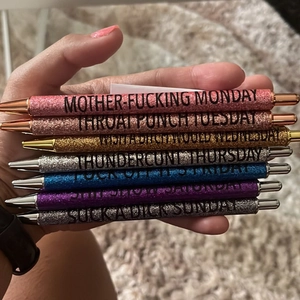 Handheld view of seven colorful glitter pens featuring bold humorous weekday phrases