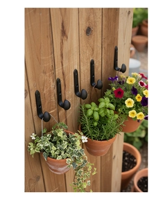 Row of black cast iron J-hooks mounted on a wooden wall for hanging garden clay pots