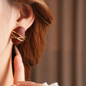Close-up of model wearing oval dark brown matte earrings with gold spiral accents