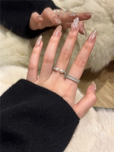 Detail of stacked pearl ring and zircon band worn on hand against plush background