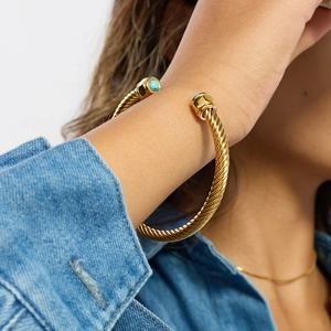 Close-up of golden twisted cuff bracelet with turquoise stones worn on a wrist