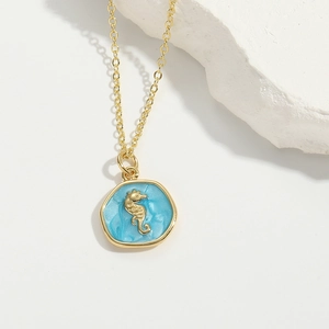 Macro view of gold seahorse pendant with light blue enamel on a minimalist gold chain