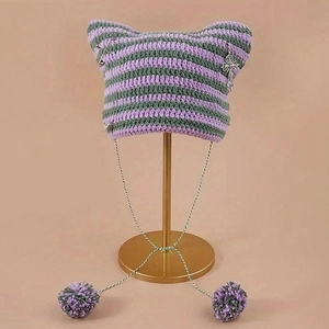 Dettaglio del cappello a maglia a righe viola e verdi con croce in metallo e spilla