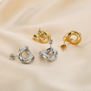 Close-up of gold and silver irregular geometric earrings on soft beige satin fabric