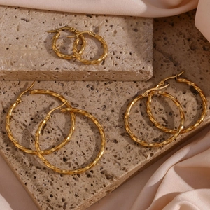 Detailed view of three sizes of gold-plated twisted hoop earrings on textured stone