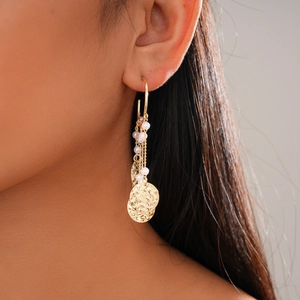 Detailed view of gold tassel earrings with pearls and hammered metal discs on model