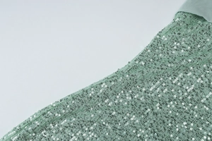 Close-up of light green sequin fabric showing sparkling texture and silver shimmering detail