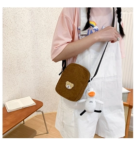Close-up of brown corduroy mini crossbody bag with cute bear embroidery and duck charm