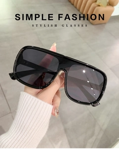 Fashionable oversized black frame sunglasses worn by a model in a modern indoor setting
