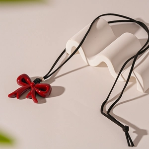 Detailed close-up of glossy red resin bow pendant with black cord on a wavy art prop