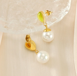 Vue détaillée macro de boucles d'oreilles dorées avec œil de chat vert et perles blanches