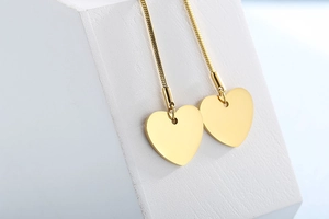 Close-up of golden heart earrings with snake chain on white geometric stand
