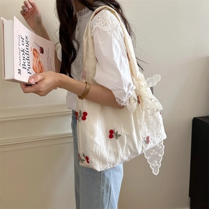 Close-up of cream canvas tote bag with red cherry embroidery and white lace bow detail