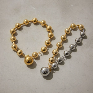 Bracelet chaîne à billes minimaliste en or 18k et argent sur surface en pierre grise
