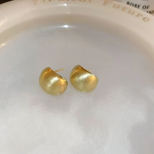 Macro shot of gold-plated C-shaped matte brushed metal earrings on ceramic plate