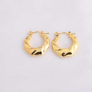 Macro detail of gold geometric twisted earrings on textured background with metallic shine