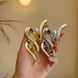 Detail showing two wave-shaped metal hair claws in gold and silver with pearl accents