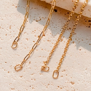 Detail of gold-plated square paperclip and rolo chains hanging on travertine stone