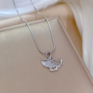 Macro shot of silver ginkgo leaf pendant on a sleek snake chain over silk fabric