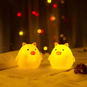 Close-up of two warm yellow pig night lights on a soft glowing background