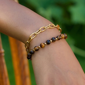 Close-up of layered gold chain and tiger eye stone beads bracelet on a woman wrist
