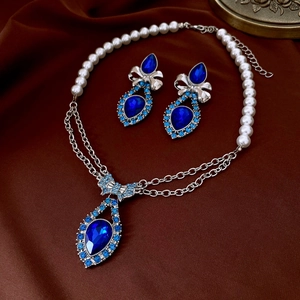 Close-up of blue teardrop gemstone and pearl necklace jewelry set on silk fabric