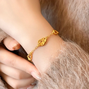 Nahaufnahme eines vergoldeten Armbands mit hohlen Blumen- und Kürbis-Anhängern auf Pullover