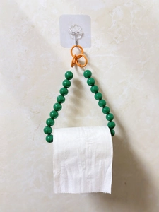 Vertical view of green beaded toilet paper holder with orange ring on marble wall
