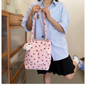 Detail of pink corduroy bucket bag with strawberry print and a white bear charm accessory