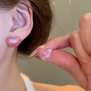 Pink heart-shaped resin stud earrings with glitter finish worn by a model