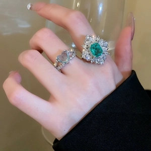 Close-up of vintage emerald cut green stone and blue heart ring with pavé diamonds