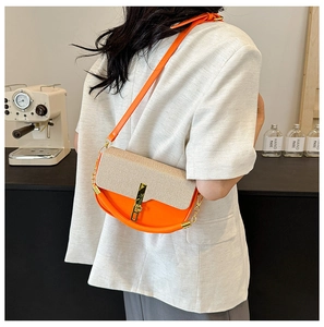 Style shot of an orange PU leather crossbody bag with beige fabric lid and gold chain strap