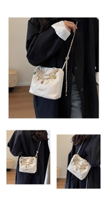Detail of white quilted bucket bag featuring colorful enamel charms and gold chain strap