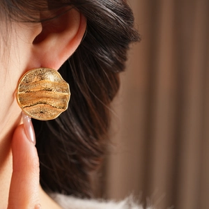 Gros plan de boucles d'oreilles rondes plissées plaquées or portées par un mannequin