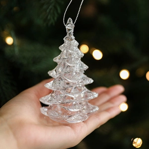 Hand holding clear acrylic Christmas tree ornament with white glitter snow and silver string