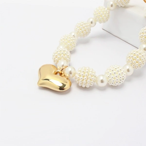 Macro shot of gold heart pendant and pearl necklace showing detailed texture and polish