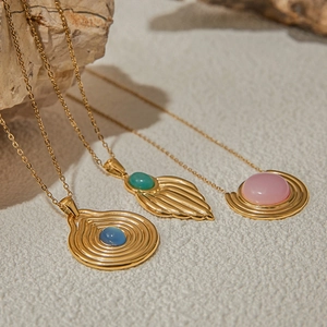 Makroansicht goldener Anhänger mit Türkis und rosa Steinen auf einem steinigen Hintergrund