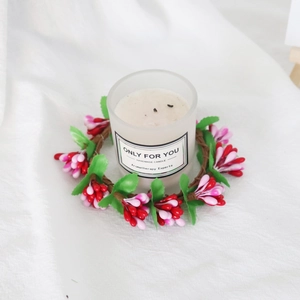 Aromatherapy candle in frosted glass with red and pink berry wreath on white fabric