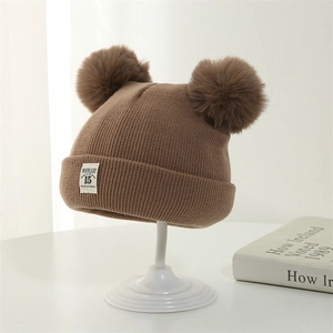Detail of brown knitted baby winter hat with double pom poms and moonlight woven label