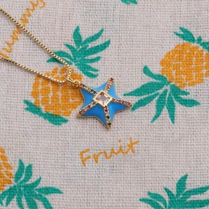Macro shot of blue enamel star pendant with colorful stones and gold box chain details