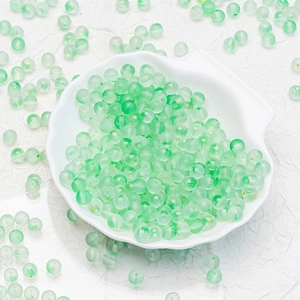 Macro shot of 6mm translucent green frosted glass beads in a white shell dish for DIY jewelry