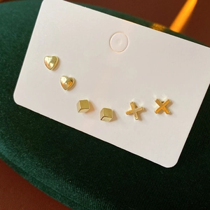 Detail of three pairs of minimalist gold geometric heart cube and cross earrings set