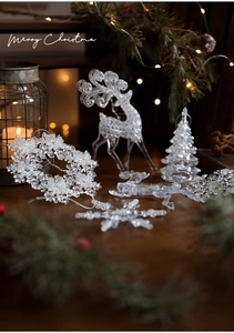 Close-up of transparent acrylic reindeer and snowflake ornaments on wooden table with bokeh lights