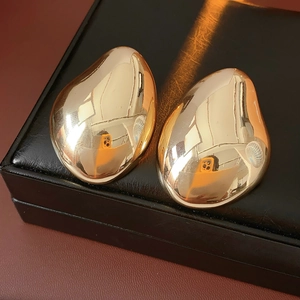 Polished golden drop earrings resting on a black leather jewelry box background