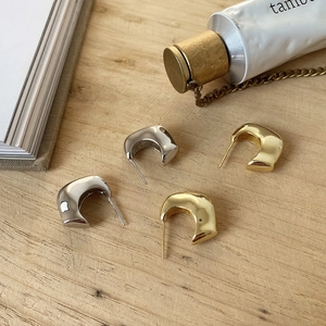 Dettaglio macro di orecchini minimalisti a forma di C color oro e argento lucido specchio