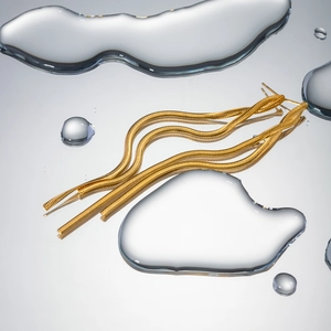 Macro shot of gold long snake chain tassel earrings on reflective water droplet surface