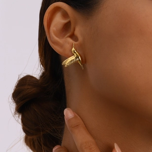 Close-up of a gold hummingbird stud earring worn by a model with detailed metallic texture