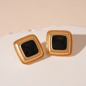 Macro shot of square gold earrings with black enamel inlay on white display stand
