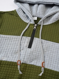 Detail of grey and green hoodie with waffle texture, metal zipper and leather cord adjusters